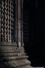 Stone steps lead up to an ornately carved doorway with intricate vertical columns, partially covered in shadow, creating a dramatic and mysterious atmosphere.