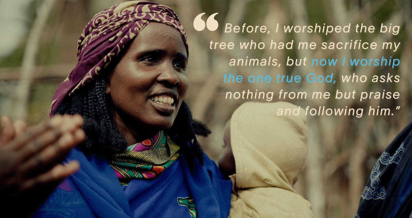 A woman wearing a patterned headscarf smiles while holding a child. Overlaid text reads: “Before, I worshiped the big tree who had me sacrifice my animals, but now I worship the one true God, who asks nothing from me but praise and following him.”.